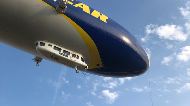 Ein Zeppelin fliegt von links nach rechts recht nah auf einen zu, man kann gut die Fahrgastkabine erkennen