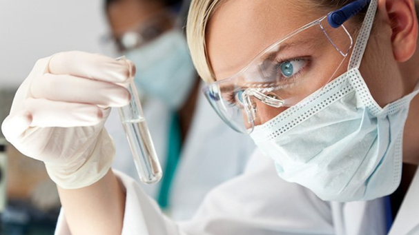 Blonde Frau mit Maske und Reagenzglas in der Hand 